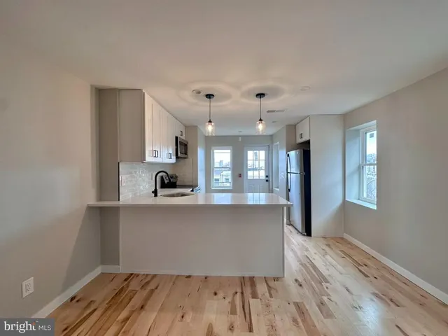 a living room with kitchen island granite countertop wooden floor stainless steel appliances cabinets and a sink