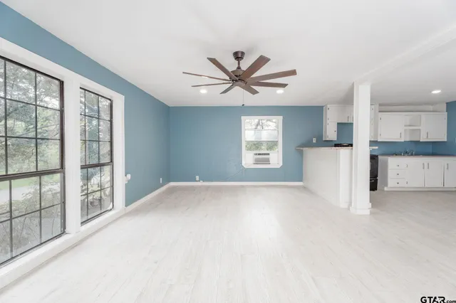 an empty room with chandelier fan and windows