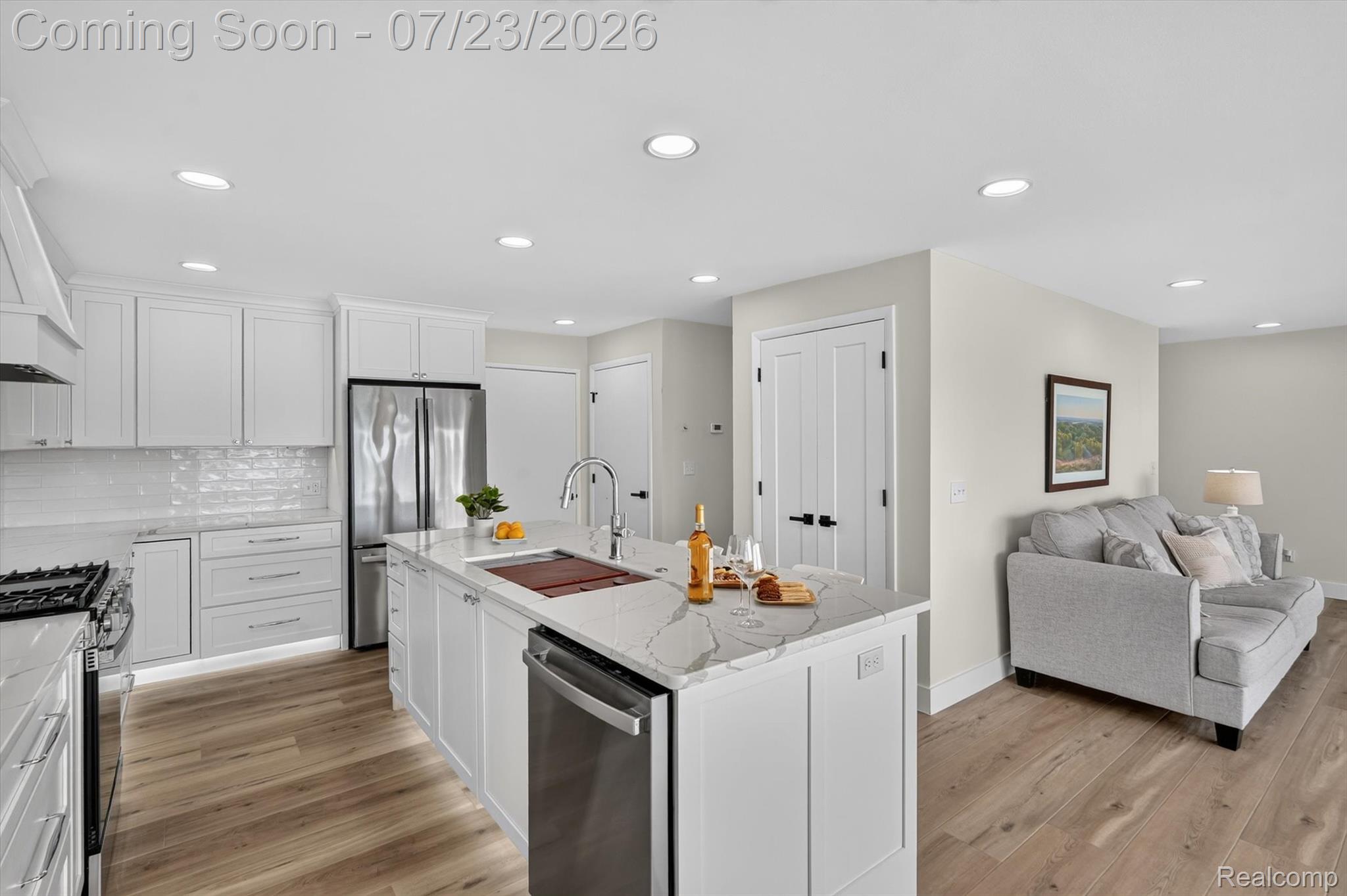 3429 Rolston Road Fenton, MI 48430 - Photo 6 of 62 Modern kitchen featuring a large island with an undermount sink, white shaker cabinetry, stainless steel appliances, and wood-finish flooring
