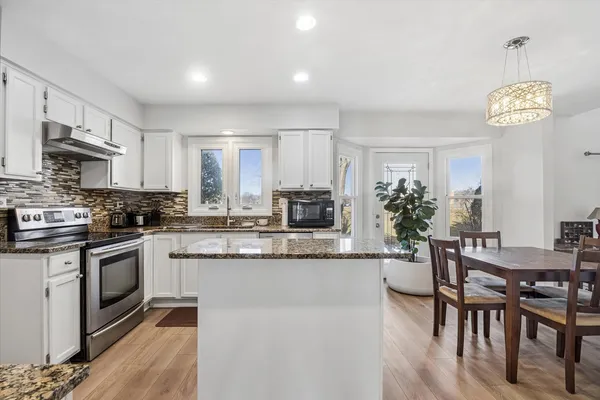 a kitchen with granite countertop a stove a sink a dining table and chairs