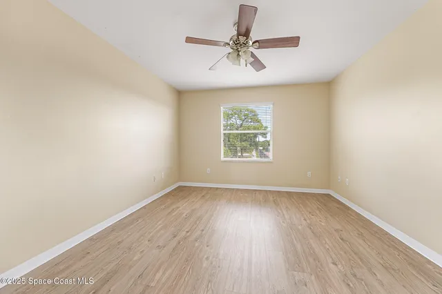 an empty room with wooden floor ceiling fan and windows