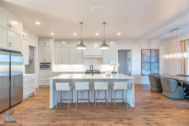 a kitchen with stainless steel appliances kitchen island granite countertop a table chairs sink and cabinets