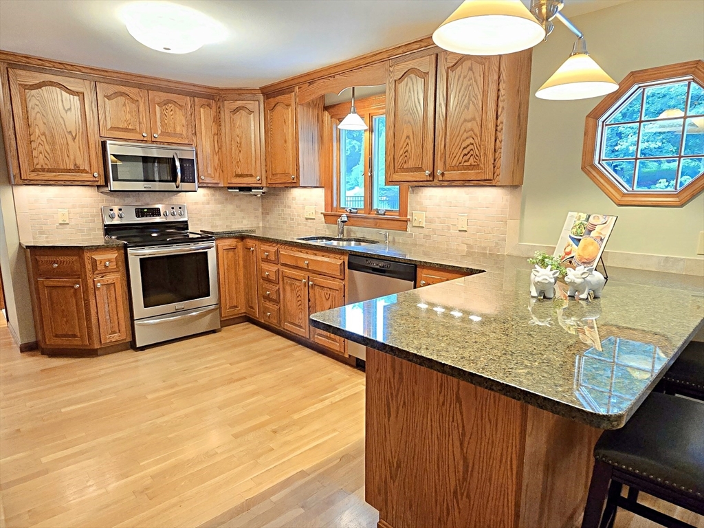 42 Wayside Lane Ashland, MA 01721 - Photo 20 of 40 a kitchen with stainless steel appliances granite countertop a sink dishwasher stove and microwave with wooden cabinets