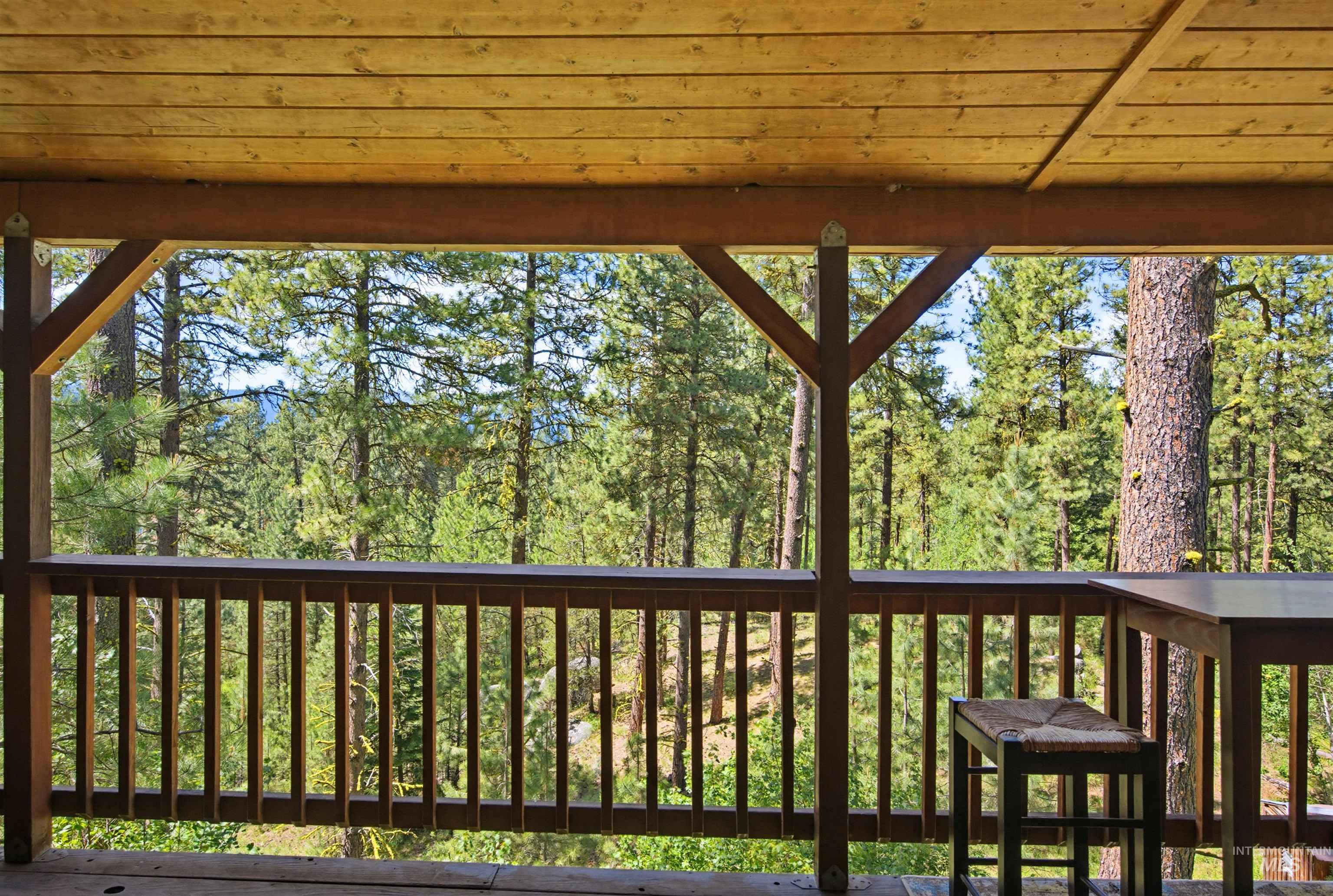 79 Sunset Loop Cascade, ID 83611 - Photo 19 of 44 Covered outdoor deck with wood panel ceiling, wood railing, structural wood beams, and a natural wooded backdrop
