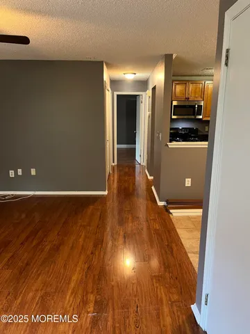 a view of a hallway to an empty room with wooden floor and a window
