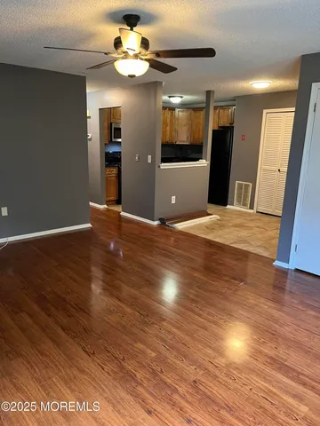 a view of an empty room with wooden floor and a kitchen