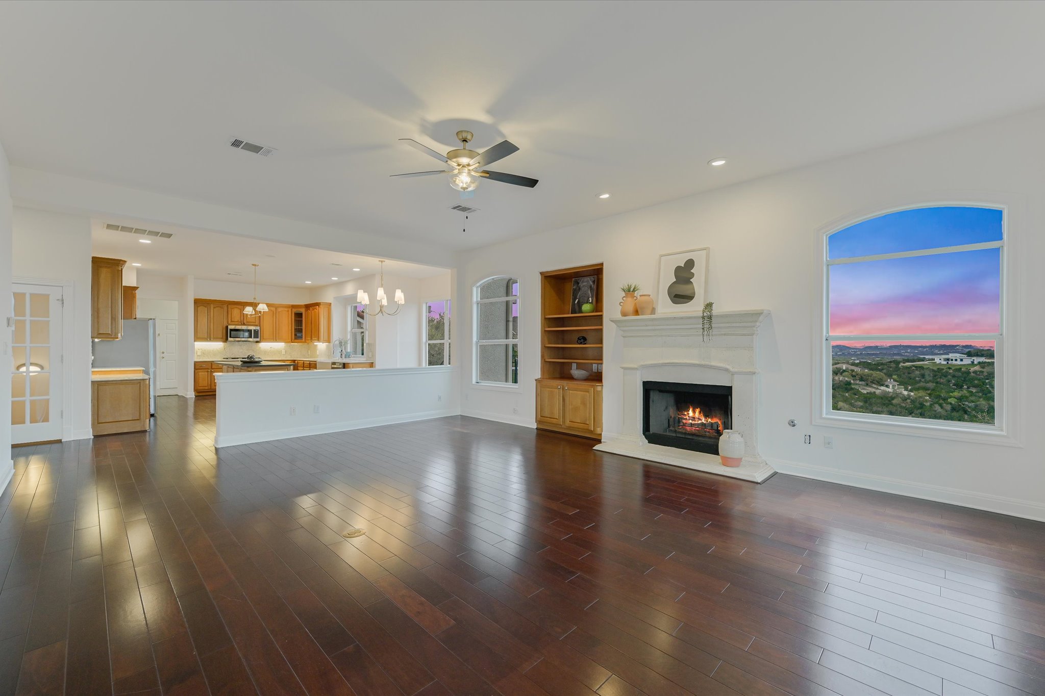 4319 Rum Runner Road Austin, TX 78734 - Photo 10 of 40 Unfurnished living room with hanging lights, a ceiling fan, a lit fireplace, and dark wood-style flooring