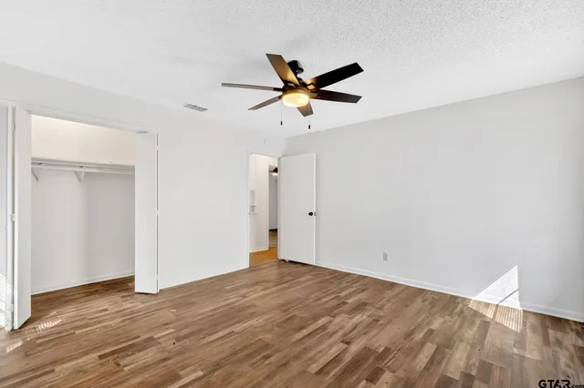 an empty room with wooden floor fan and windows