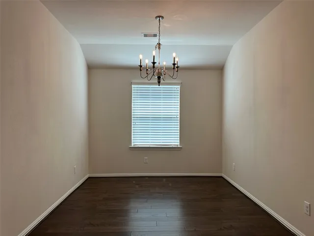 an empty room with wooden floor chandelier and windows