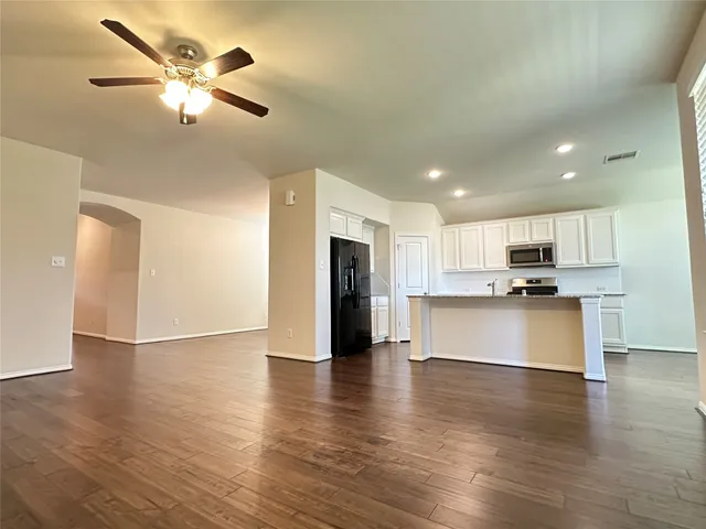 a view of an empty room with kitchen appliances and a ceiling fan