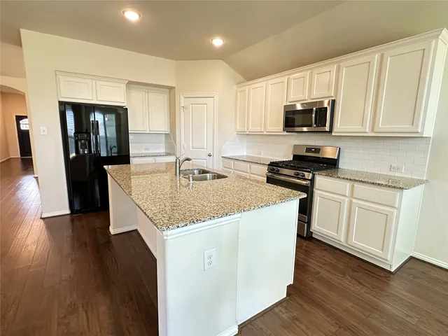 a kitchen with stainless steel appliances granite countertop a stove top oven a sink dishwasher and a refrigerator with wooden floor