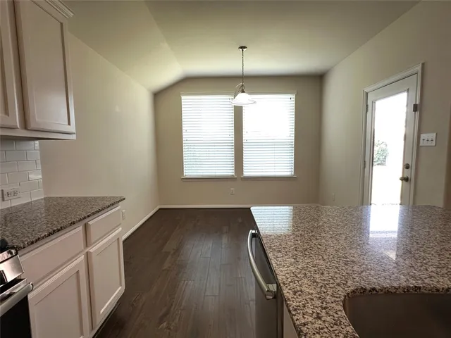 an empty room with wooden floor a kitchen view and windows