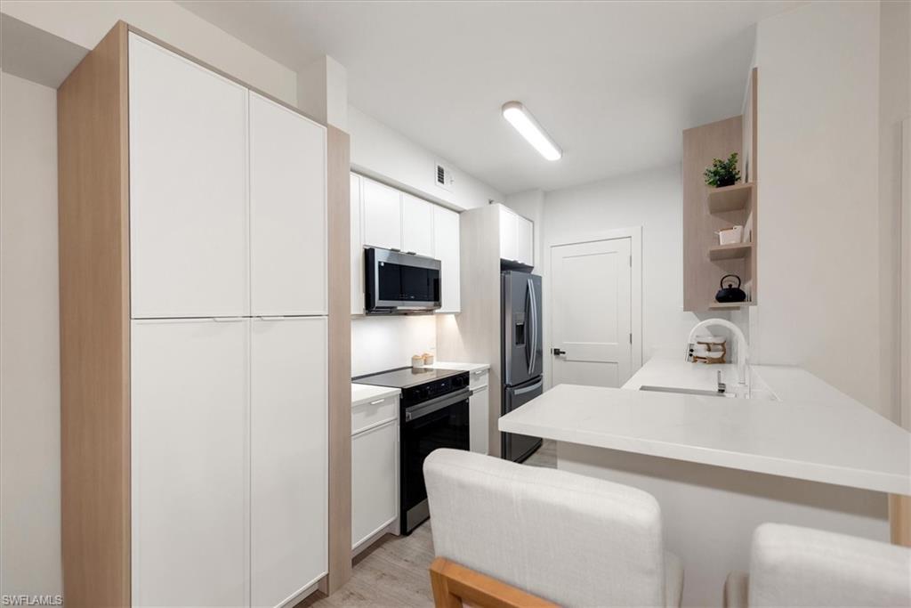1170 Reserve Way, Unit 107 Naples, FL 34105 - Photo 5 of 47 Kitchen with appliances with stainless steel finishes, white cabinetry, a peninsula, open shelves, and light wood-style flooring