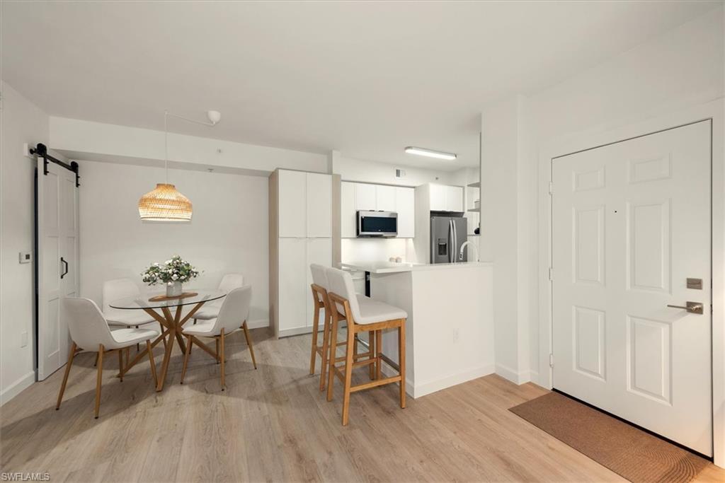 1170 Reserve Way, Unit 107 Naples, FL 34105 - Photo 9 of 47 Kitchen featuring a barn door, white cabinets, a breakfast bar area, light wood finished floors, and light countertops