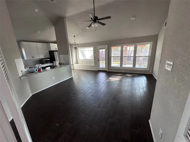 an empty room with wooden floor a ceiling fan and windows
