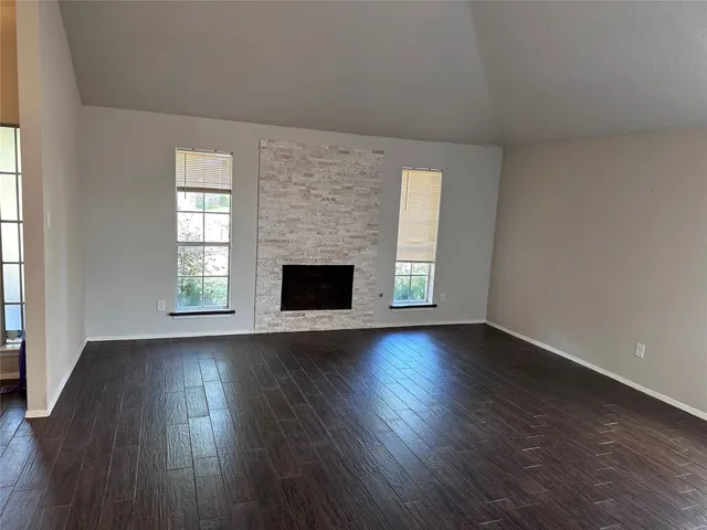 an empty room with wooden floor fireplace and windows