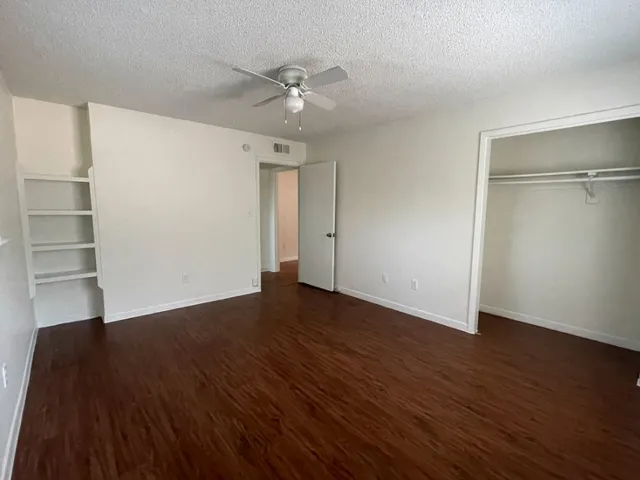 a view of an empty room with wooden floor and a ceiling fan