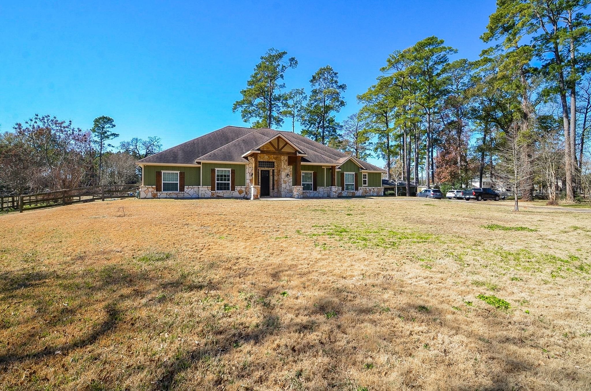 13327 Little Ranch Road Cypress, TX 77429 - Photo 1 of 49 A front view of this single-story home shows it set on a spacious lot with mature trees and a wide open lawn. The exterior features green siding with stone accents and a covered entry, all under a natural, lightly clouded sky. The property offers privacy, space, and a peaceful setting.