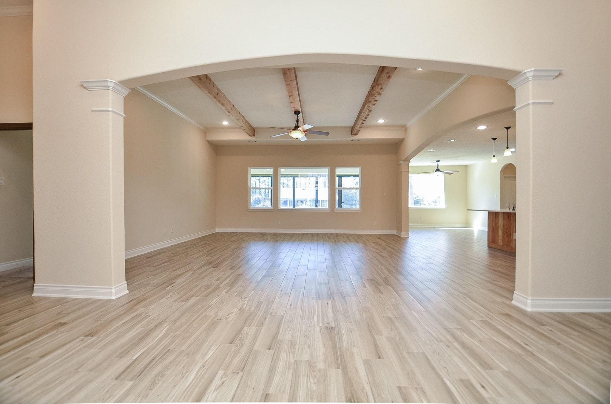 13327 Little Ranch Road Cypress, TX 77429 - Photo 12 of 49 This spacious living room features an open-concept layout with high ceilings and elegant arched openings. Exposed wood beams add character and warmth, while the wide-plank flooring and neutral tones create a bright, inviting atmosphere. Large windows provide natural light and views of the outdoors, making the space ideal for both everyday living and entertaining.