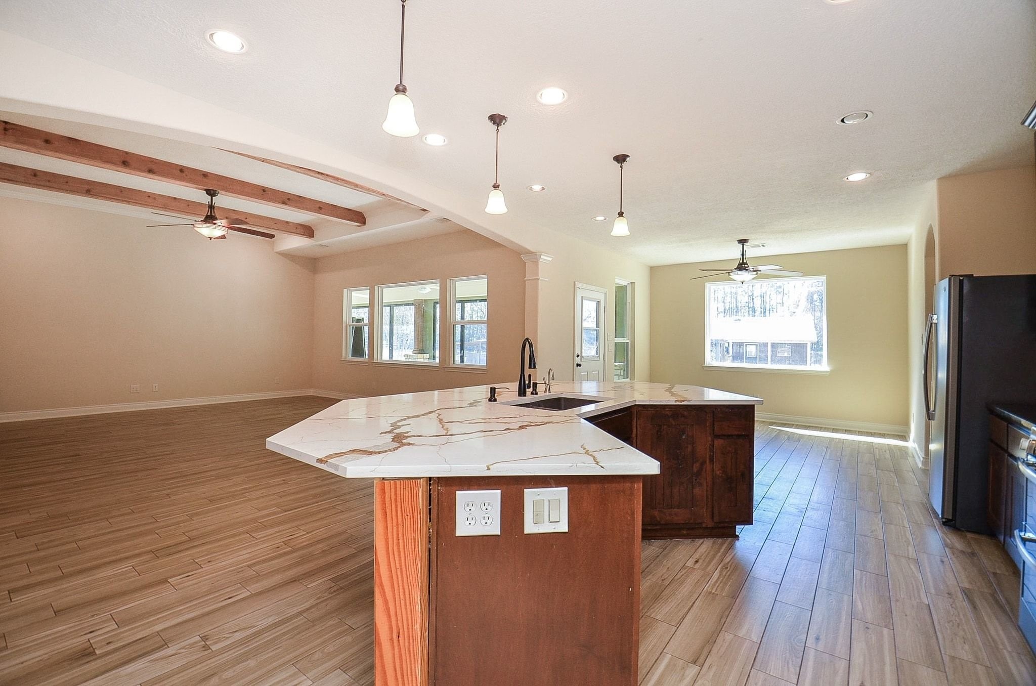 13327 Little Ranch Road Cypress, TX 77429 - Photo 17 of 49 This photo showcases a spacious open-concept kitchen and living area. It features modern pendant lighting, a large island with a marble countertop, and wood-beamed ceilings. The room is bright with ample natural light from multiple windows, complemented by wood-look tile flooring.