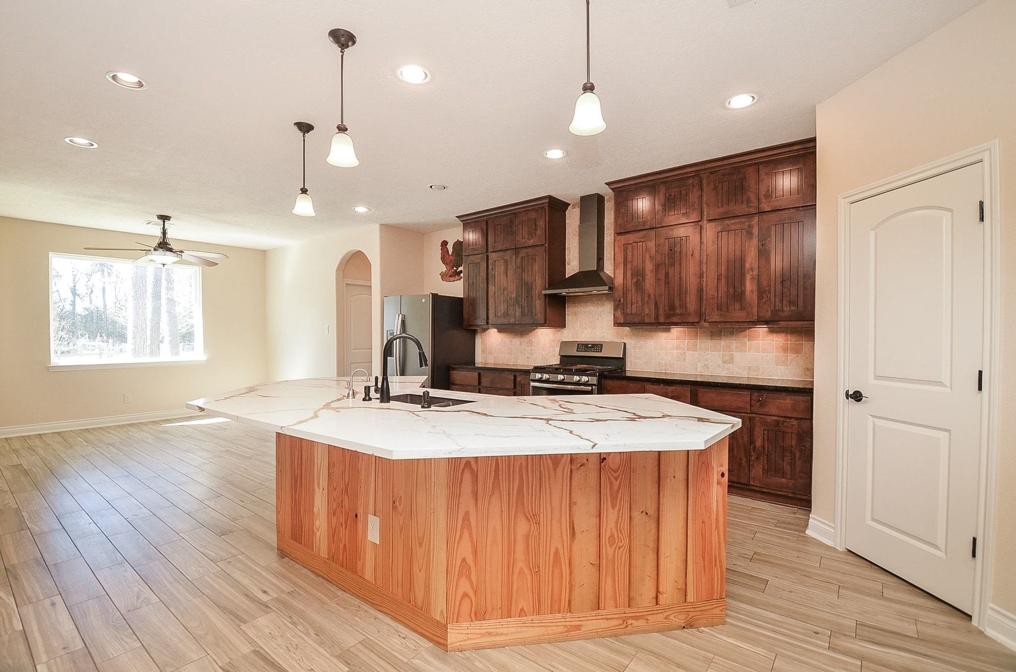 13327 Little Ranch Road Cypress, TX 77429 - Photo 18 of 49 This bright, open-concept kitchen features a large marble island with a modern sink and fixtures, dark wood cabinetry, and stainless steel appliances. The adjacent dining area has ample natural light and wooden flooring, creating a warm and inviting space.