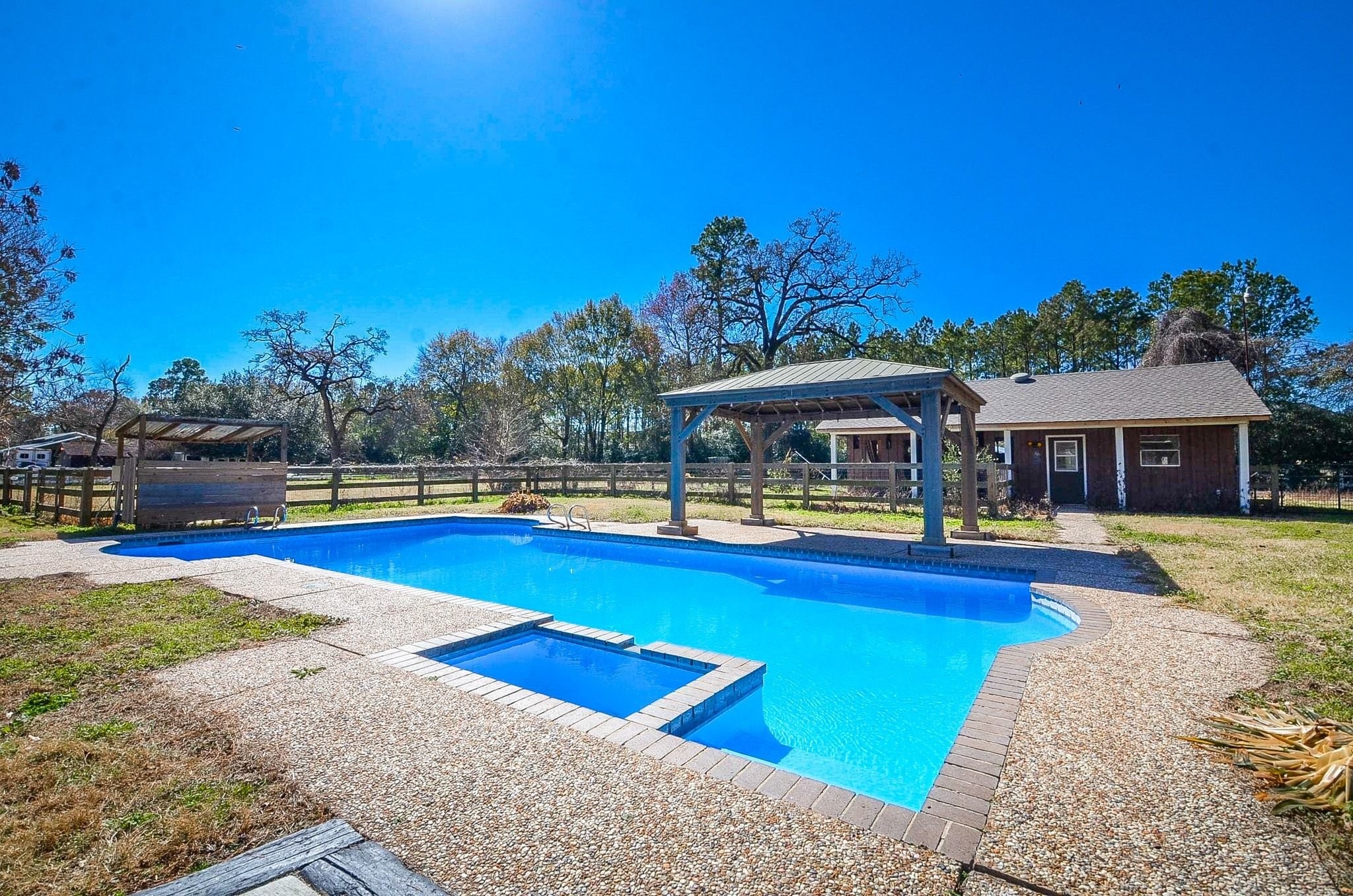 13327 Little Ranch Road Cypress, TX 77429 - Photo 3 of 49 This property features a spacious backyard with a large in-ground swimming pool, a covered patio area, and a rustic outbuilding. It's surrounded by a wooden fence and lush trees, offering privacy and a serene outdoor experience.