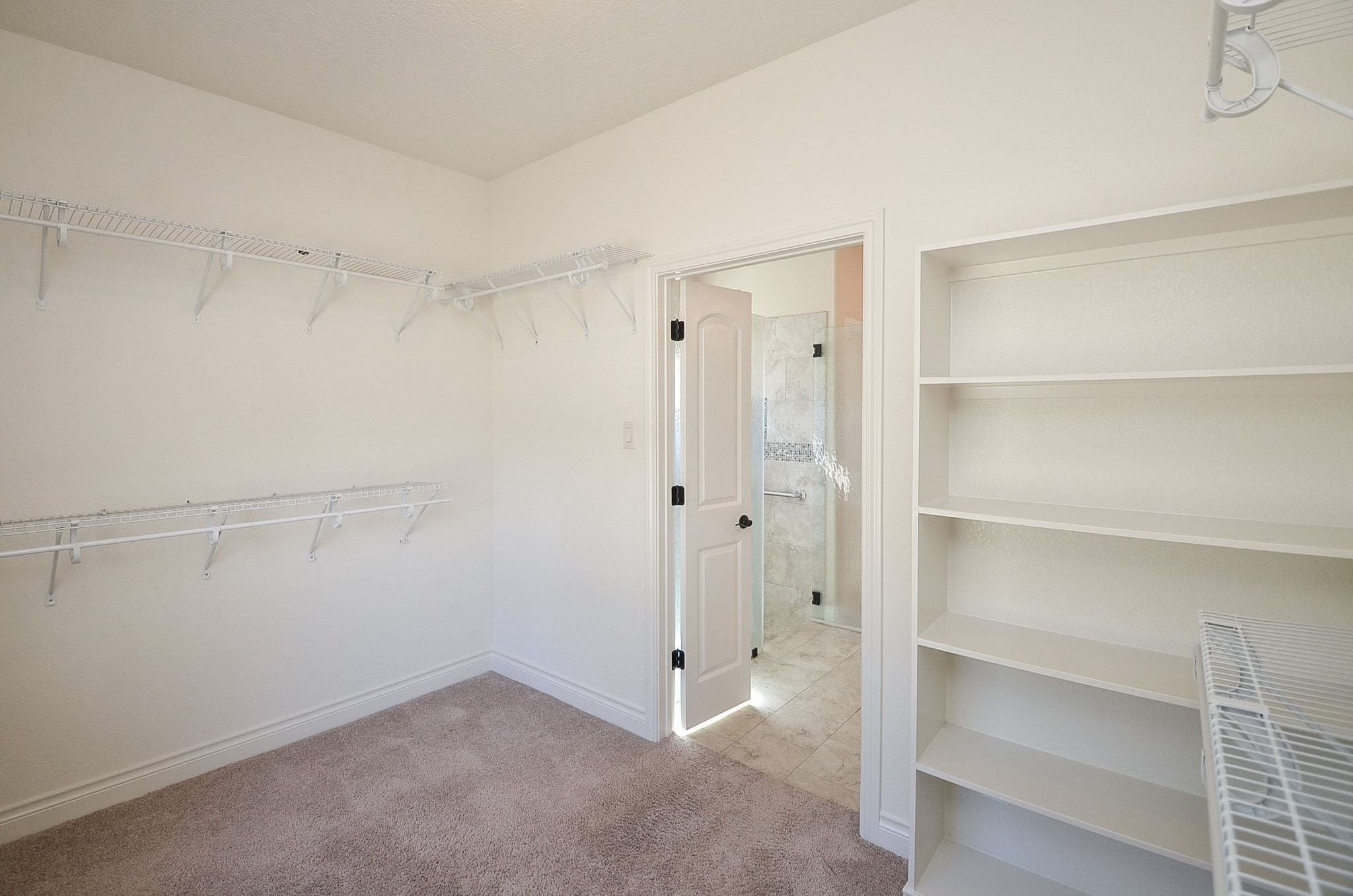 13327 Little Ranch Road Cypress, TX 77429 - Photo 35 of 49 This photo shows a spacious walk-in closet with carpeted flooring, multiple wire shelves, and built-in storage. It has a door leading to an adjoining room, likely a bathroom, visible with tiled flooring.