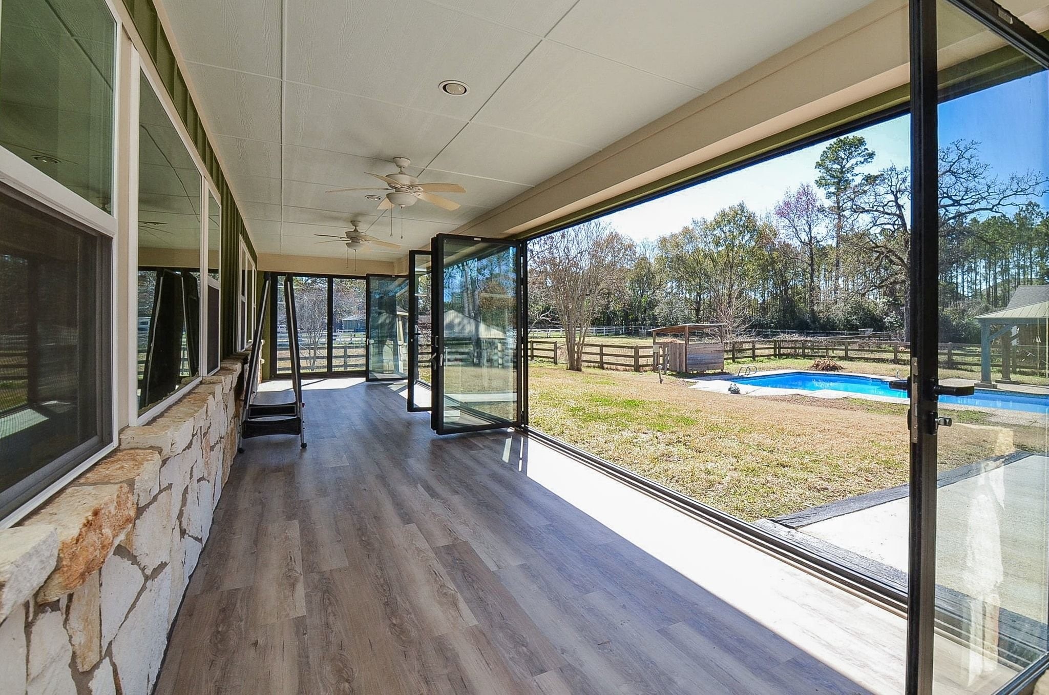 13327 Little Ranch Road Cypress, TX 77429 - Photo 39 of 49 This photo shows the folding glass door system fully opened, creating a wide, unobstructed opening that seamlessly connects the covered patio to the outdoor living space. The open design allows for abundant natural light, fresh air, and clear views of the backyard and pool, making the space ideal for entertaining and indoor-outdoor living.