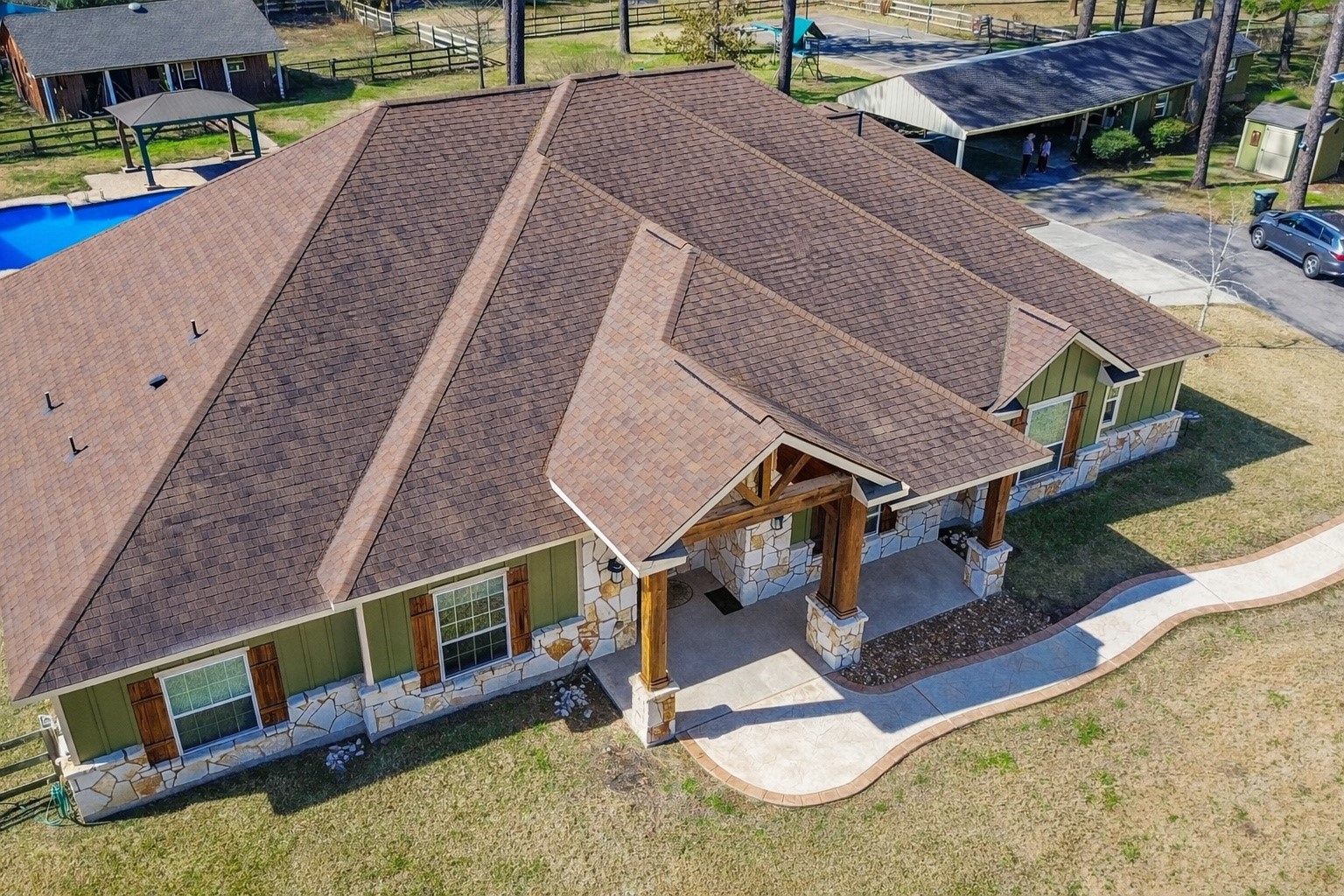 13327 Little Ranch Road Cypress, TX 77429 - Photo 6 of 49 This photo showcases a spacious single-story house with a gabled roof and stone accents. It features a large front porch and a neatly landscaped walkway. The property includes a backyard pool and appears to be in a peaceful, rural setting with ample outdoor space.