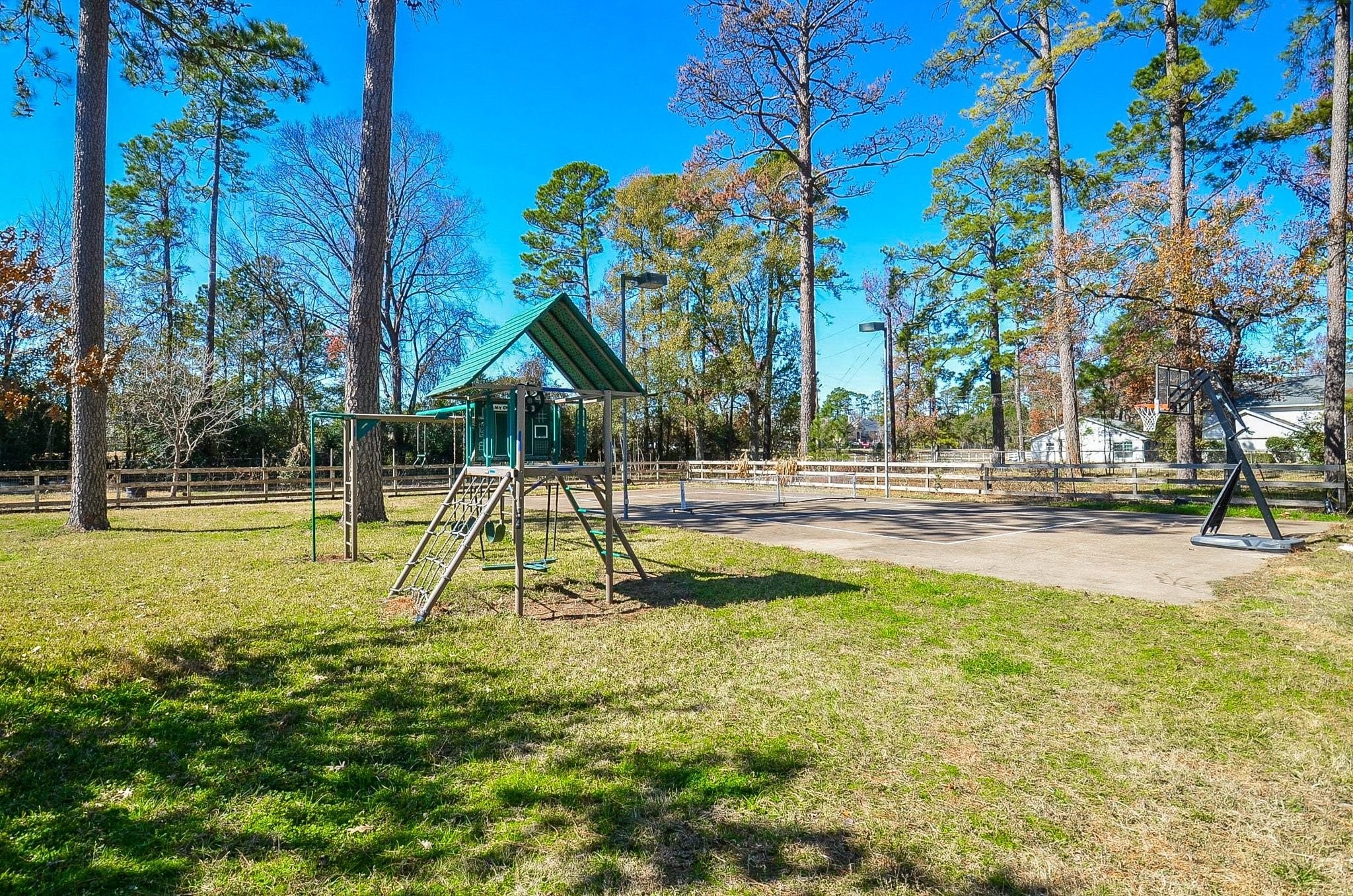 13327 Little Ranch Road Cypress, TX 77429 - Photo 9 of 49 Spacious backyard with a children's playset and a basketball hoop, surrounded by trees and a wooden fence. Perfect for family activities and outdoor enjoyment.