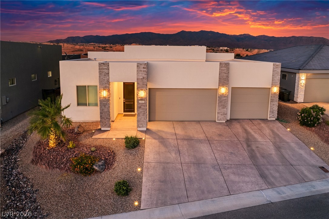 1460 Blue Ridge Trail Mesquite, NV 89027 - Photo 3 of 39 Modern desert home with a mountain backdrop, illuminated for an inviting evening presence.