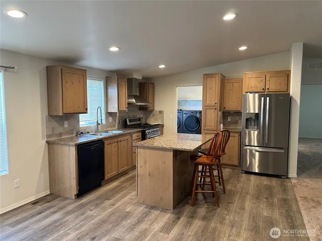 a kitchen with stainless steel appliances granite countertop a refrigerator a stove top oven a sink dishwasher and a refrigerator with wooden floor