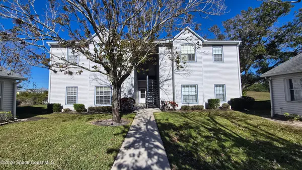a view of a white house next to a yard with a large tree