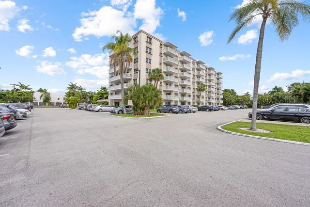 a view of a tall white building with a yard and palm trees