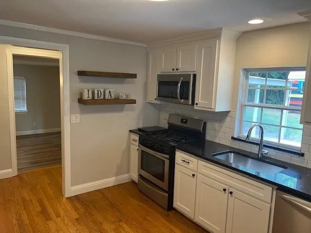a kitchen with granite countertop a sink cabinets stainless steel appliances and a window