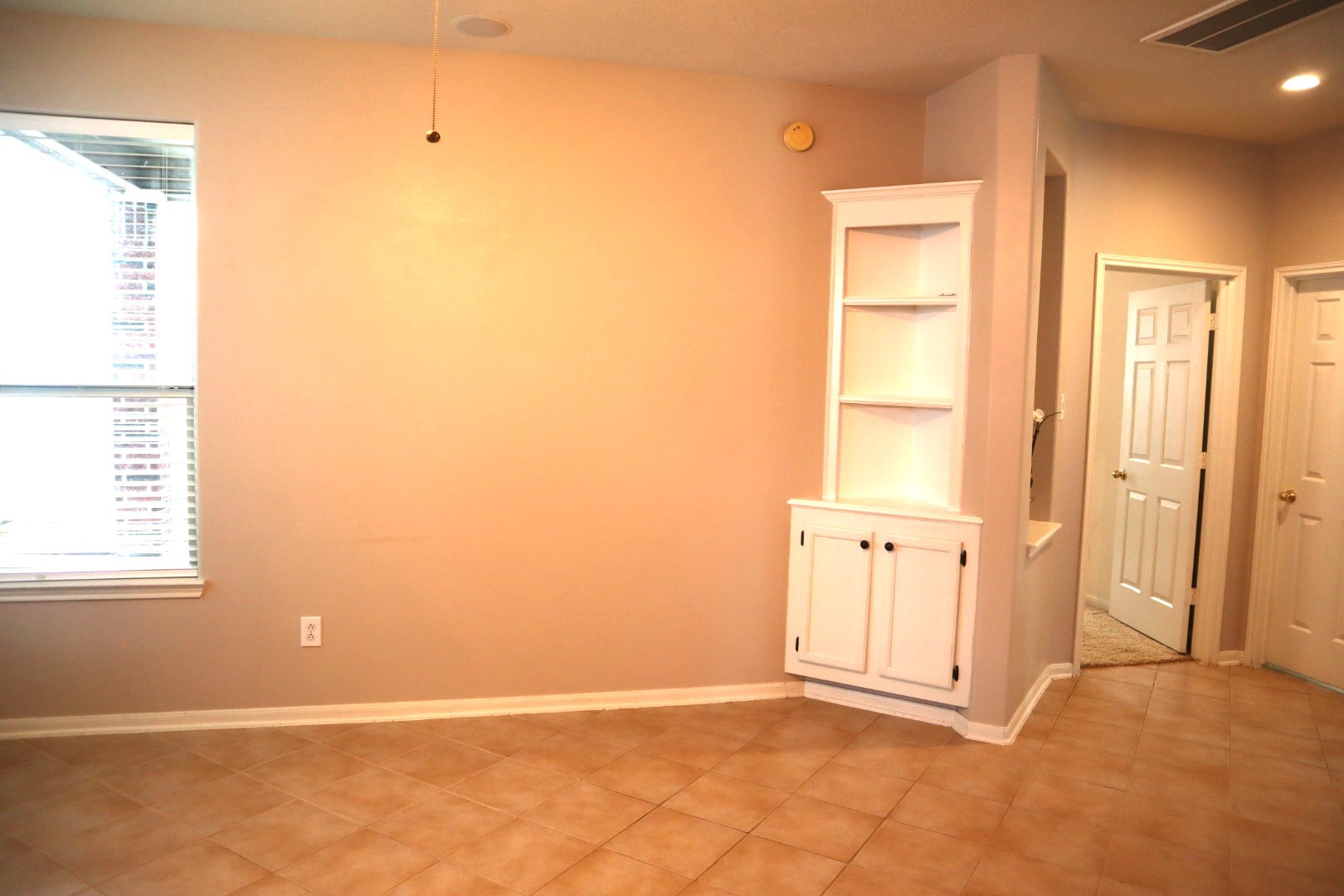 19114 Emory Trail Spring, TX 77388 - Photo 12 of 32 The Family Room features neutral-toned walls and tiled flooring, with a large window providing natural light. It includes a built-in white cabinet and shelving unit and leads to adjacent rooms through open doorways.