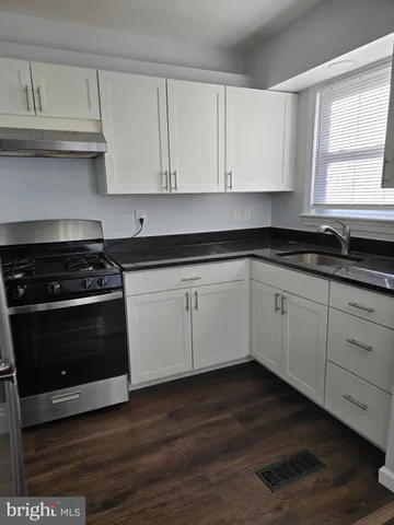 a kitchen with granite countertop white cabinets and a stove with wooden floor
