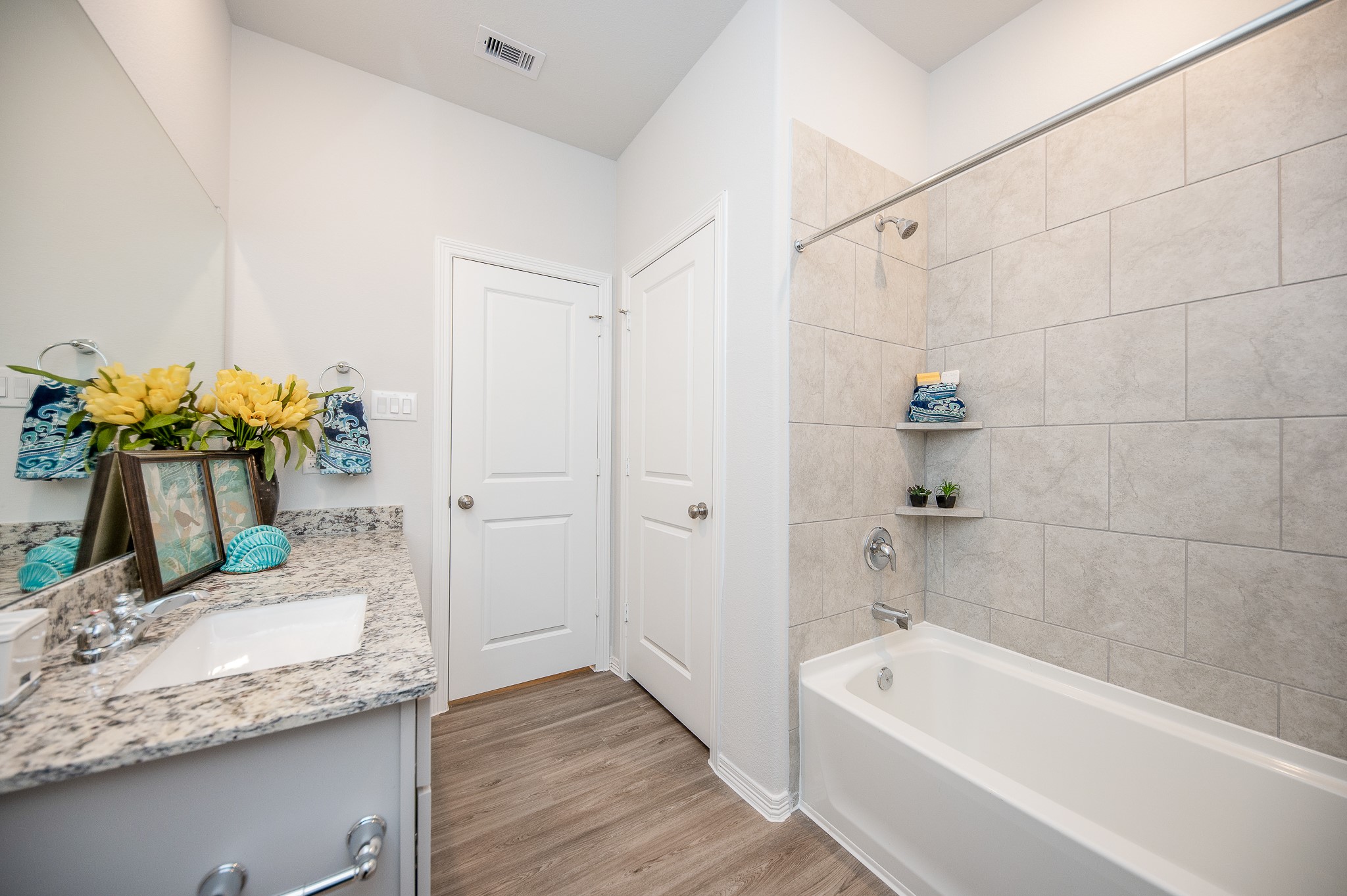 23302 Spring Genesis Lane Katy, TX 77493 - Photo 29 of 32 This bathroom features a modern design with a granite countertop, sleek sink, and a bathtub with tiled walls. The light wood flooring and bright decor create a fresh and inviting atmosphere.