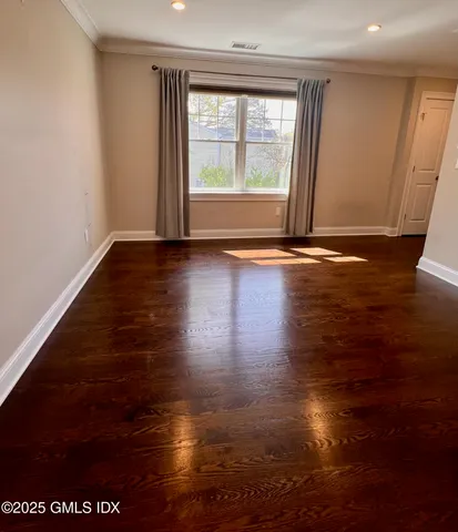 an empty room with wooden floor and windows with curtains