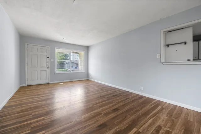 a view of an empty room with wooden floor and a window