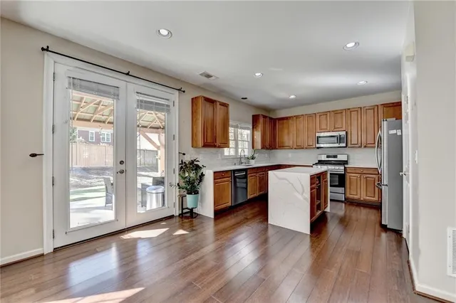 a kitchen with stainless steel appliances granite countertop a refrigerator a sink dishwasher a stove and a dining table with wooden floor