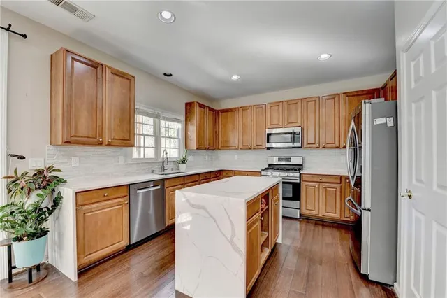 a kitchen with stainless steel appliances granite countertop a refrigerator a sink dishwasher a stove and white countertops with wooden floor