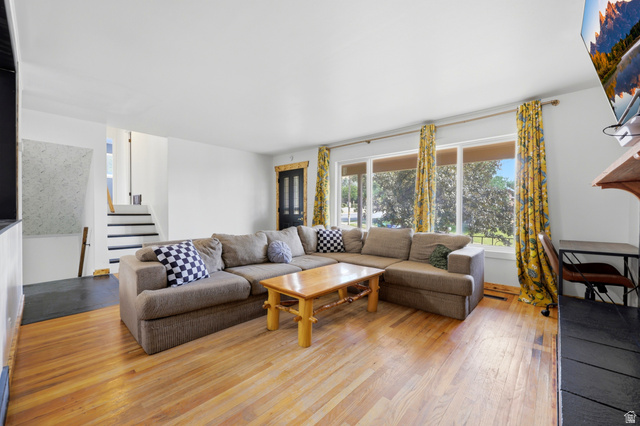 1486 3rd Street Ogden, UT 84404 - Photo 4 of 26 Spacious living area featuring expansive wood-finish flooring, a large window overlooking exterior greenery, white walls, and a staircase with dark treads