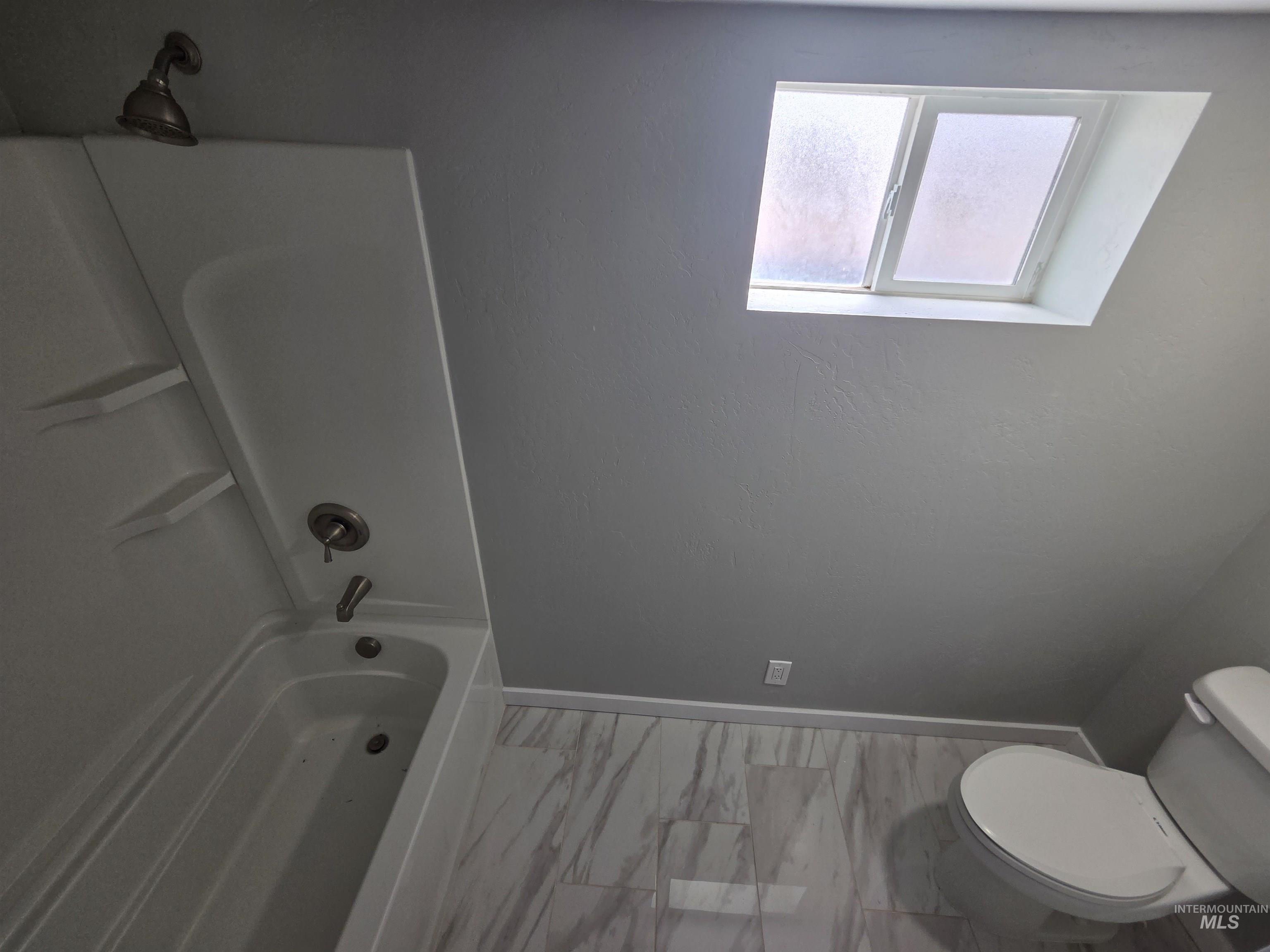 905 15th Drive Rupert, ID 83350 - Photo 13 of 20 Bathroom featuring a white bathtub and shower combination with a bronze-finish showerhead, a white toilet, and gray-veined tile flooring