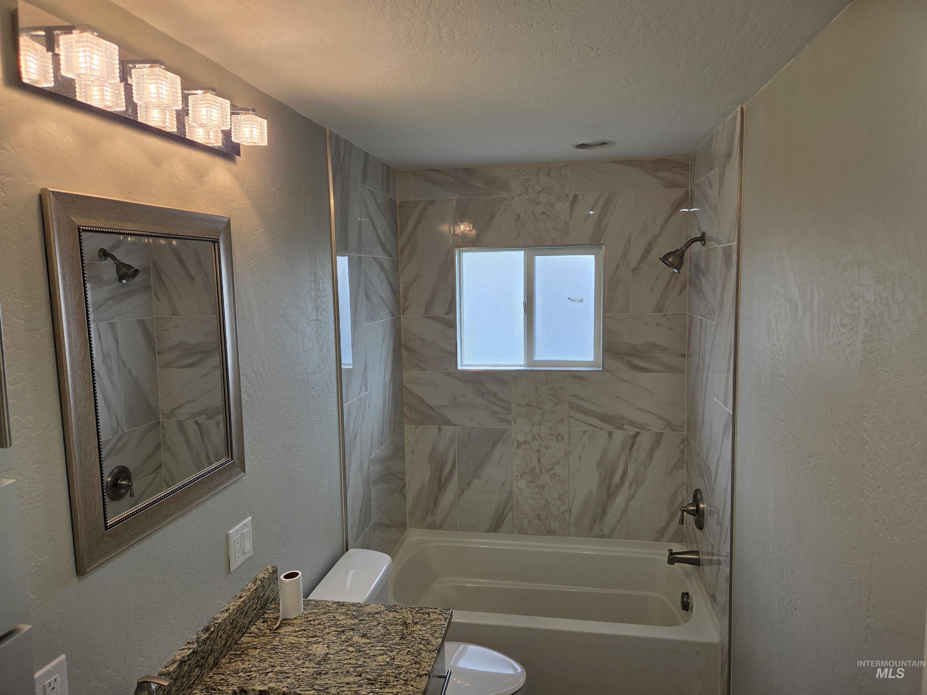 905 15th Drive Rupert, ID 83350 - Photo 6 of 20 Bathroom featuring a tub/shower combination with tile surround, a window, a vanity with a granite-finish countertop, and a framed mirror
