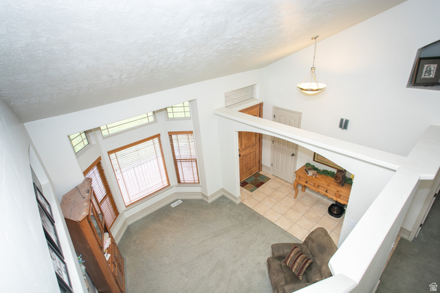 426 Deer Hollow Road Tooele, UT 84074 - Photo 4 of 37 Unfurnished living room featuring carpet, a towering ceiling, a textured ceiling, and tile patterned floors