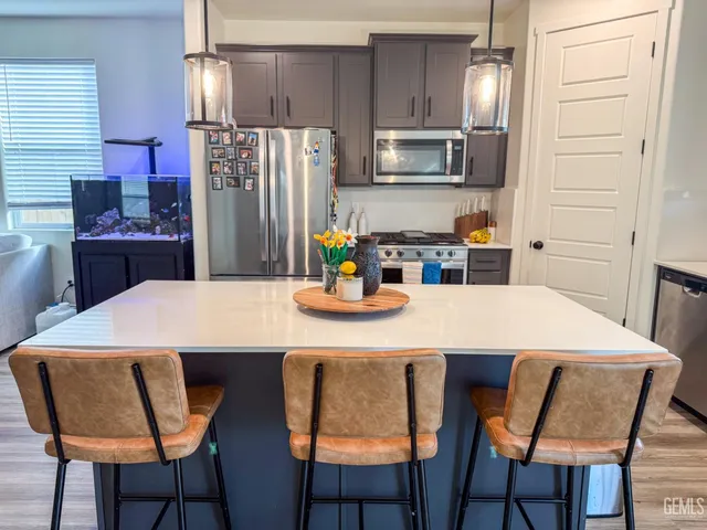 a kitchen with stainless steel appliances kitchen island granite countertop a dining table chairs and a refrigerator