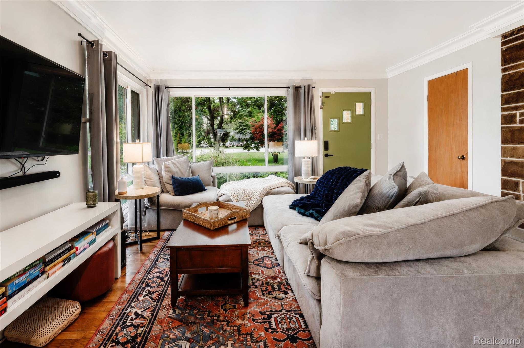 Hardwood flooring, crown molding, a stone-clad wall accent, and large windows define this living area