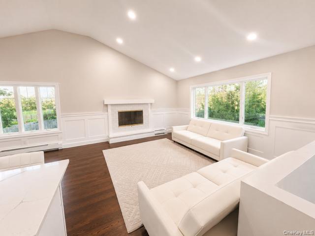 321 Sherbrooke Road Lindenhurst, NY 11757 - Photo 5 of 21 Spacious great room featuring vaulted ceilings with recessed lighting, large multi-pane windows flooding the space with natural light, a fireplace with surround, and warm wood-finish flooring throughout