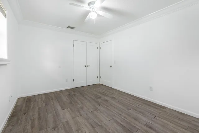 a view of an empty room with wooden floor and a ceiling fan